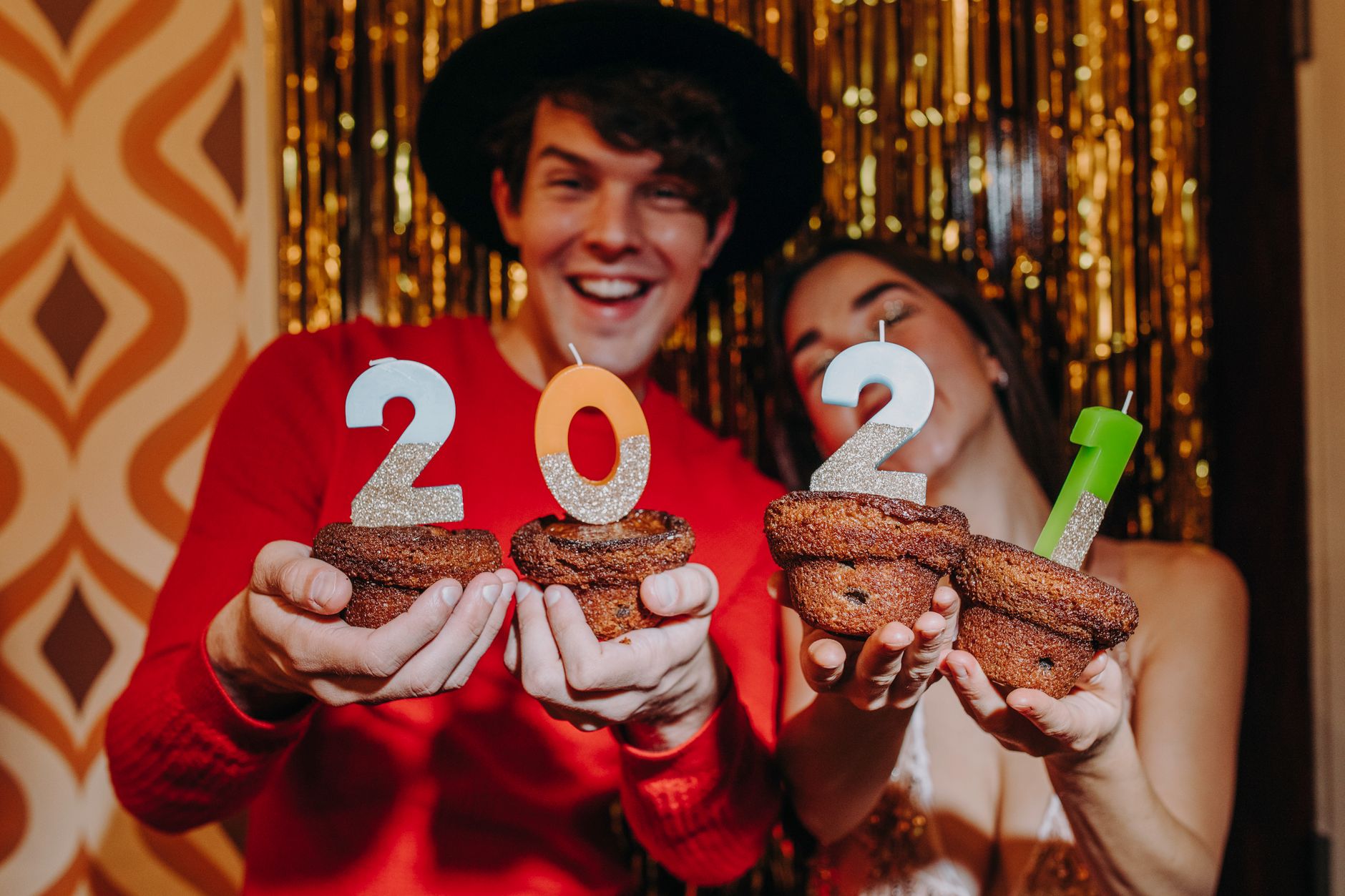 Happy couple celebrating New Year's Eve with cupcakes and 2021 candles.