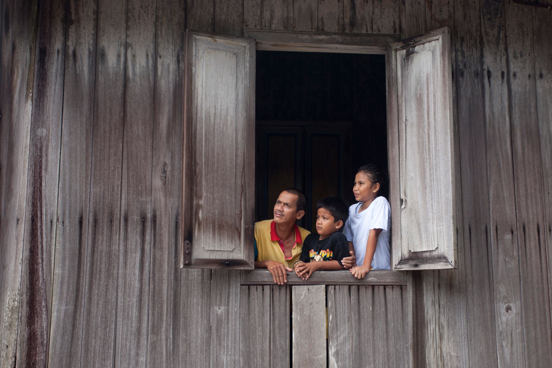Family peering out an open window of a rustic wooden house, bonding and gazing outside.